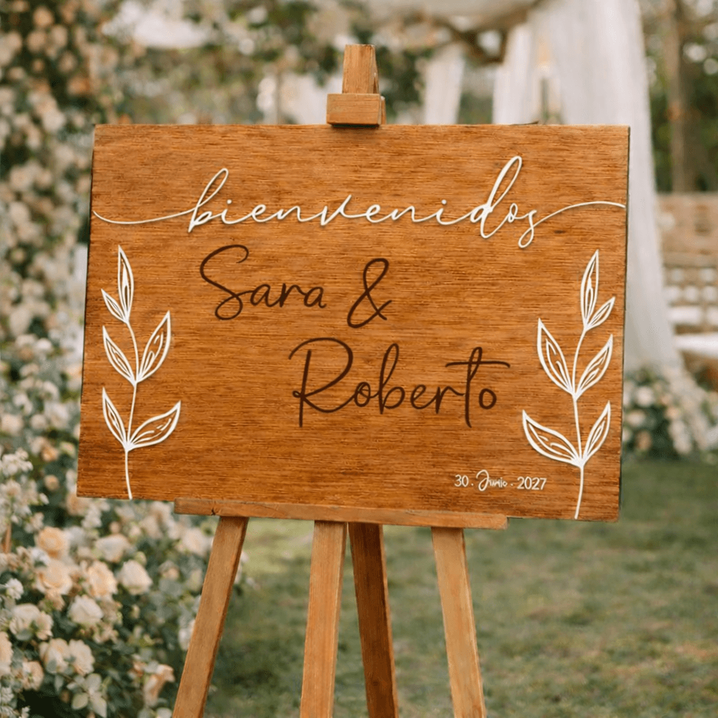 Cartel boda madera con palabra bienvenidos en relieve acrílico blanco y hojas botánicas grabadas
