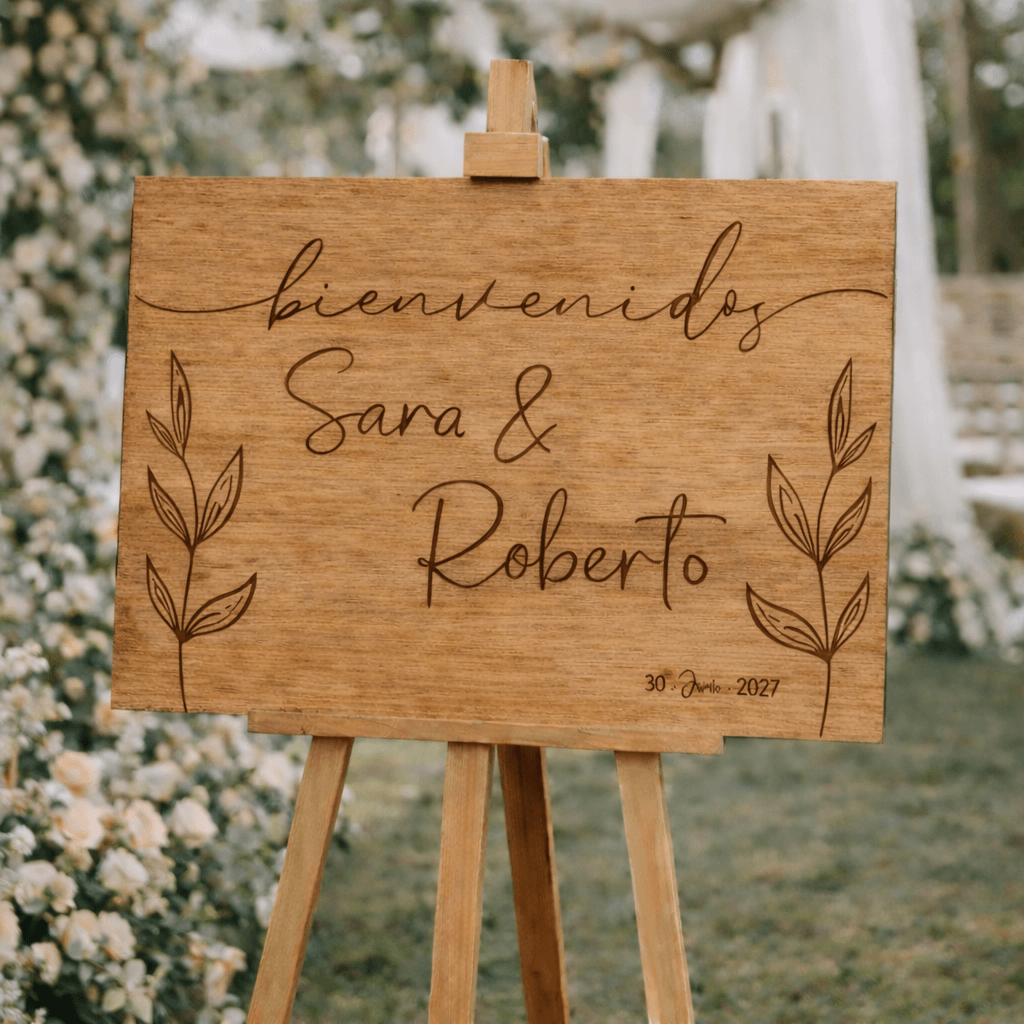 Nombres personalizados y fecha grabados en cartel de boda de madera con diseño de hojas naturales
