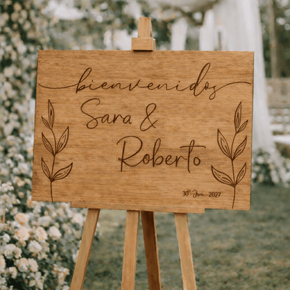Nombres personalizados y fecha grabados en cartel de boda de madera con diseño de hojas naturales
