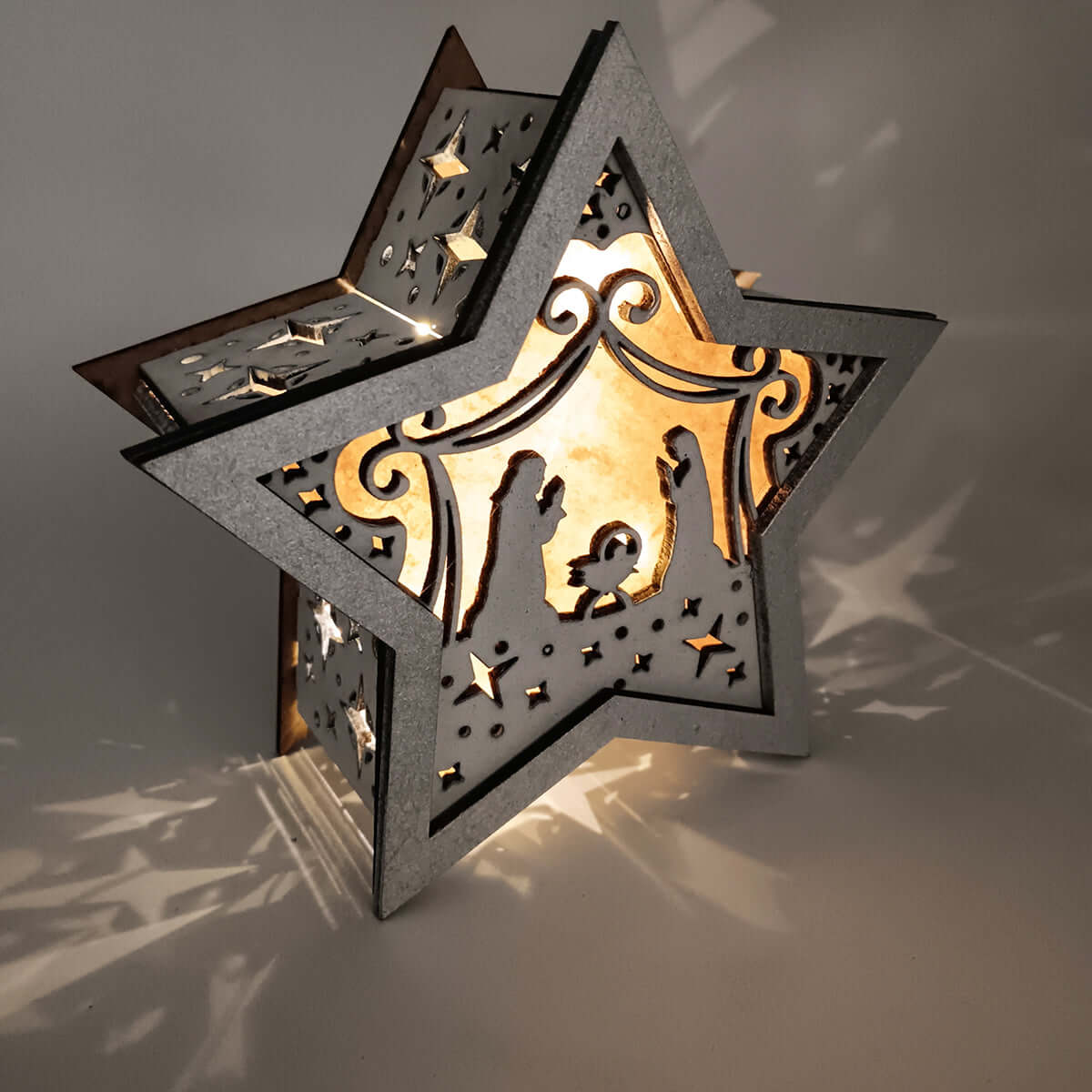 Lámpara artesanal de madera con forma de estrella y pesebre iluminado en luces LED cálidas.
